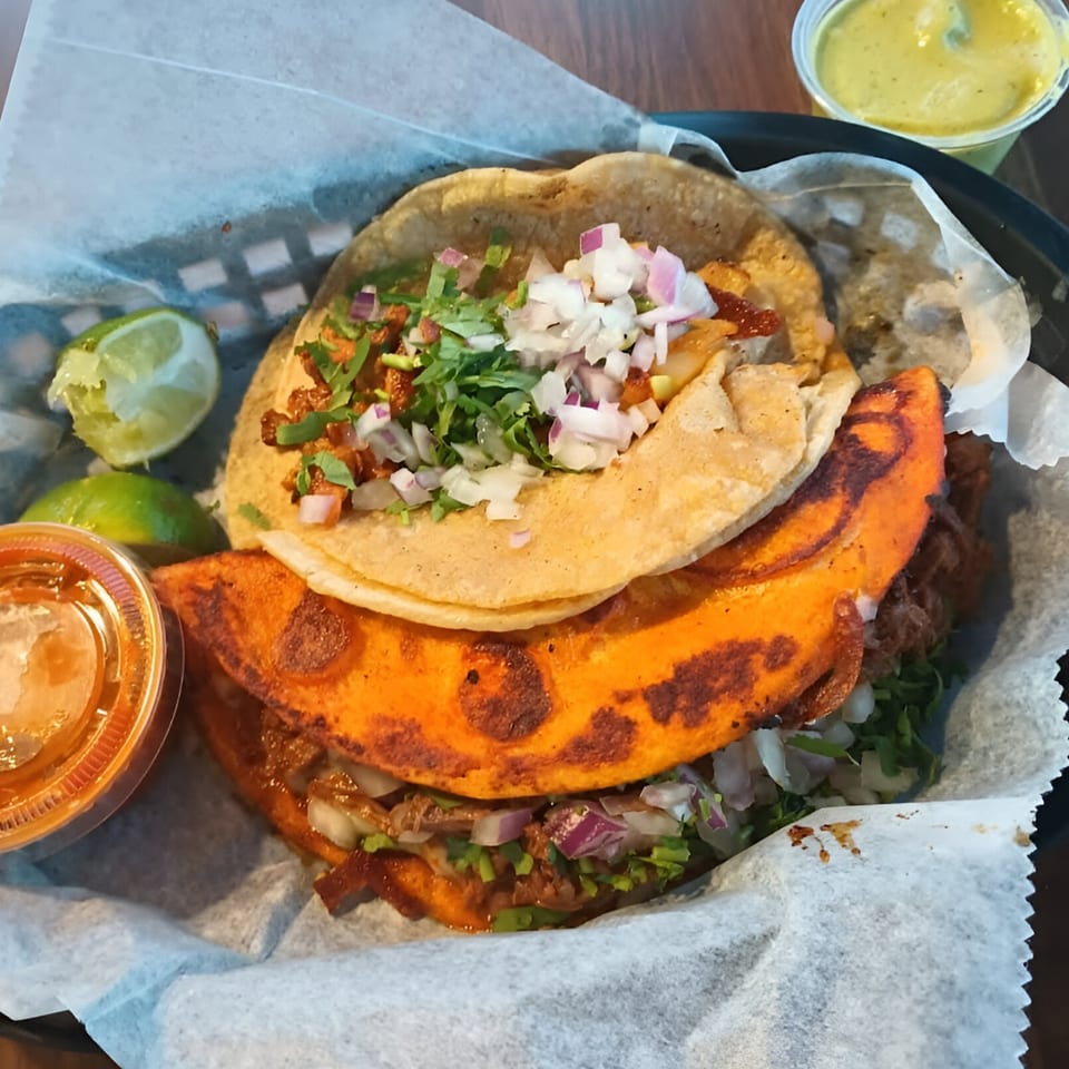 Three Sabor Mexican tacos, two birria and one al pastor, with lime wedges and sauces.