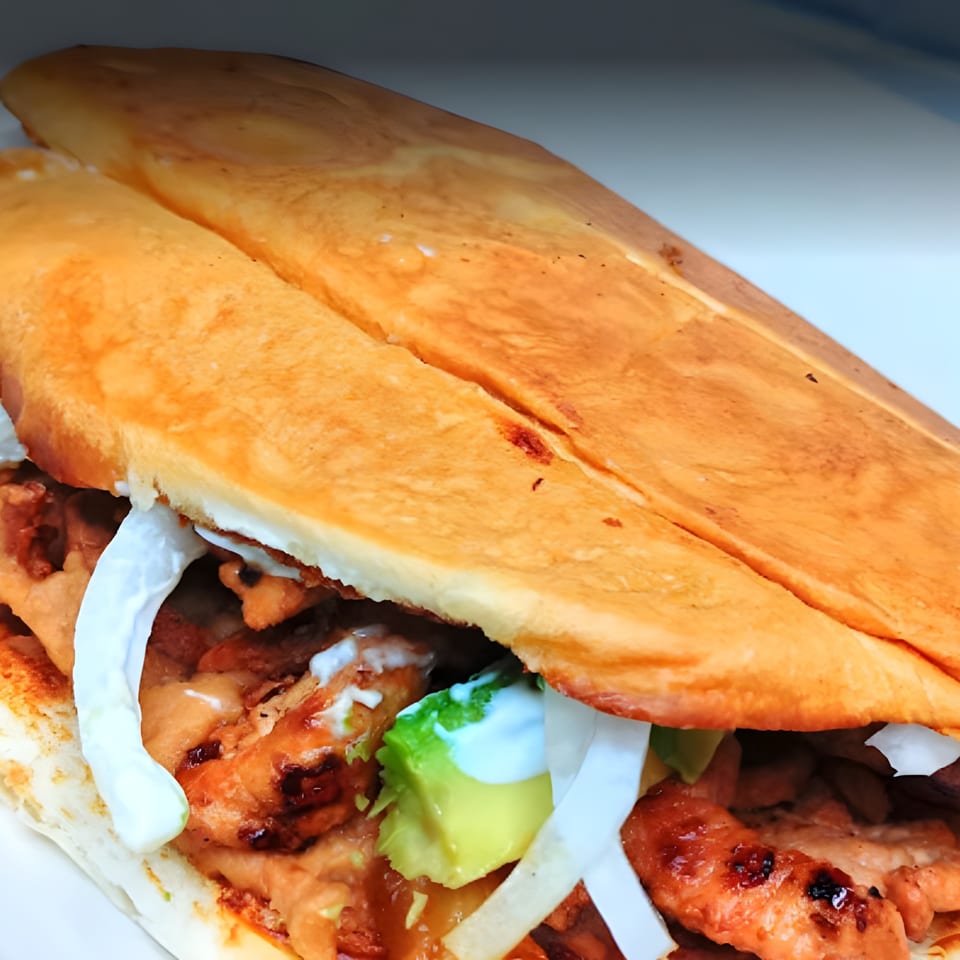 A close-up of a Mexican torta with grilled meat, avocado, onions, and crema.